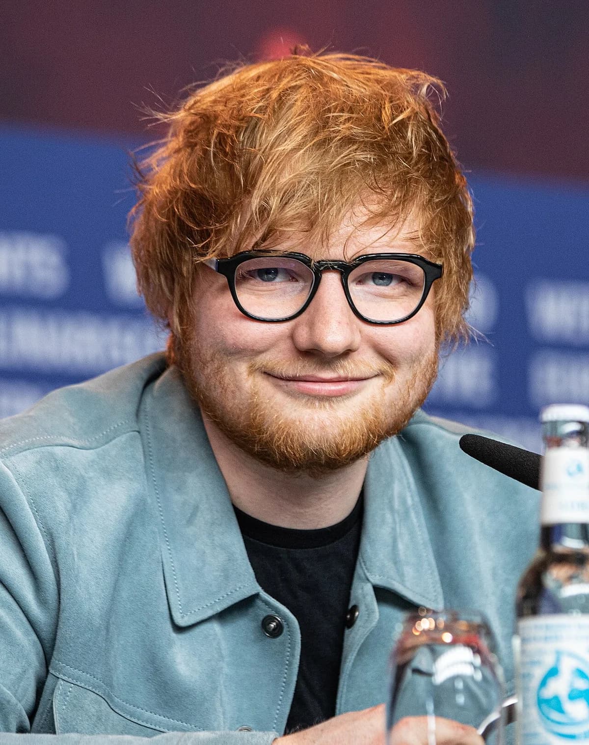 Ed Sheeran smiling with glasses at a press event