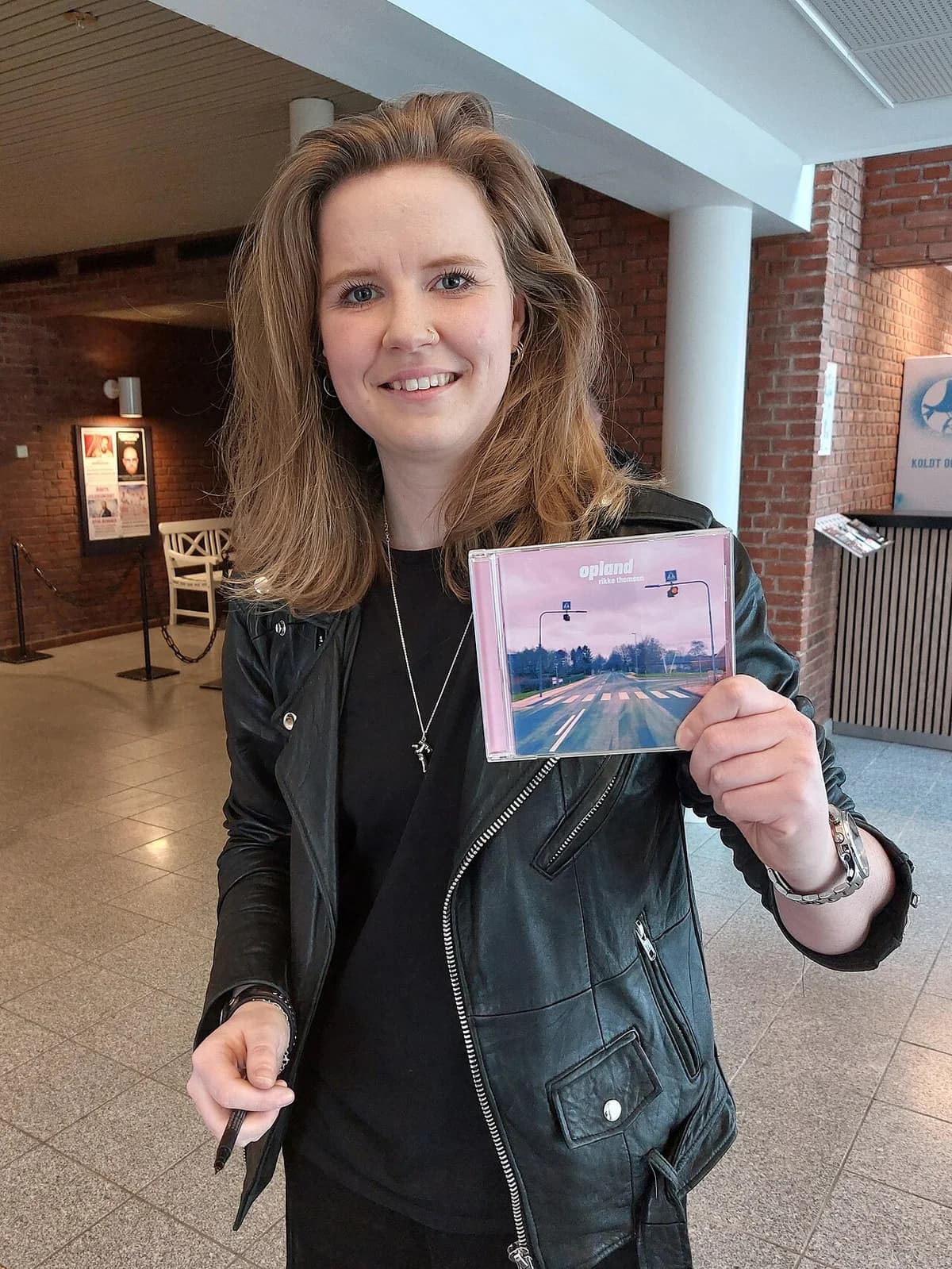 A woman holding up her new CD after a concert indoors.