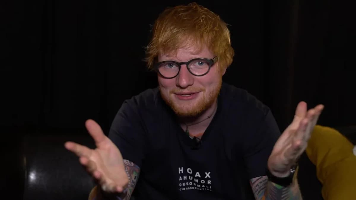 Ed Sheeran speaking and gesturing in a dark interview setting.