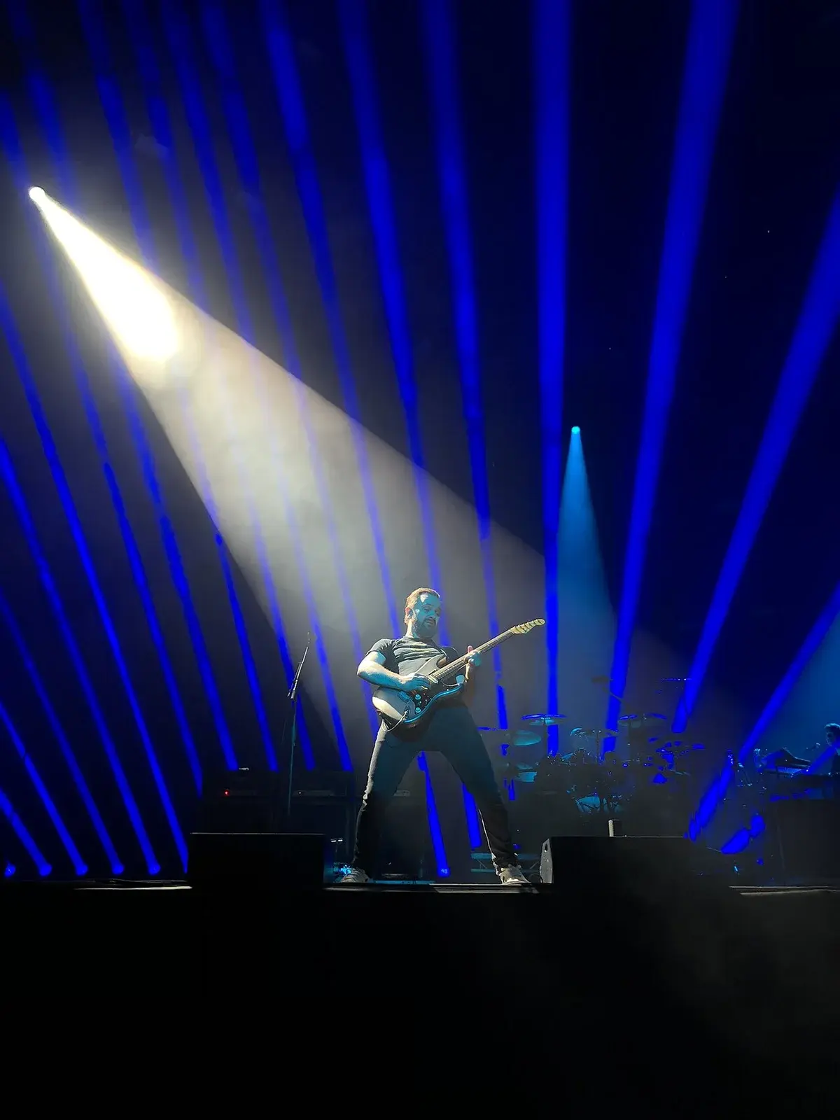 A guitarist performs under blue stage lights and a bright spotlight.