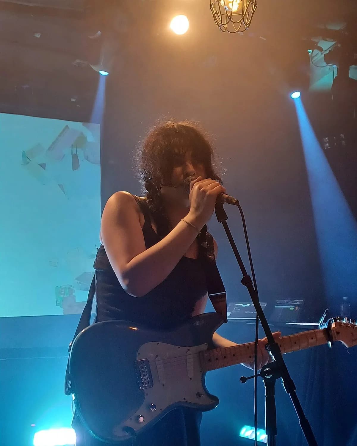 Person singing and playing electric guitar on stage with spotlights