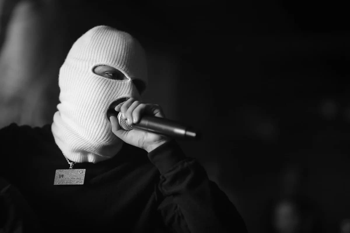 A masked musician passionately singing into a microphone during a live performance.