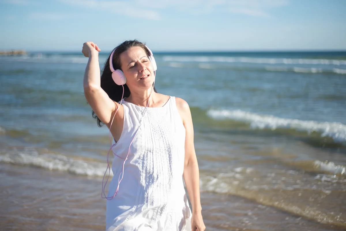 Woman wearing headphones and a white dress on a beach.