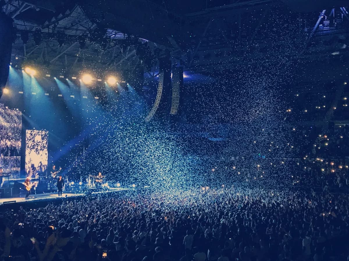 Energetic live concert with confetti and cheering crowd under bright stage lights.