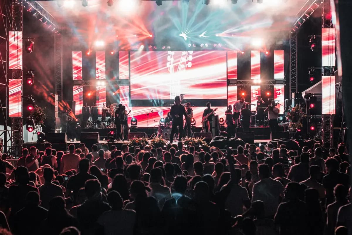 A large crowd watches an outdoor concert at night under colorful stage lights.