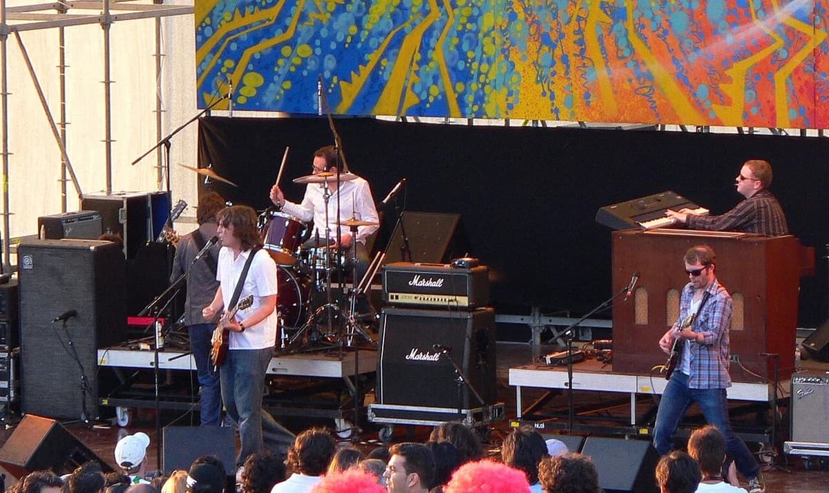 Band performing live on outdoor stage with abstract mural background