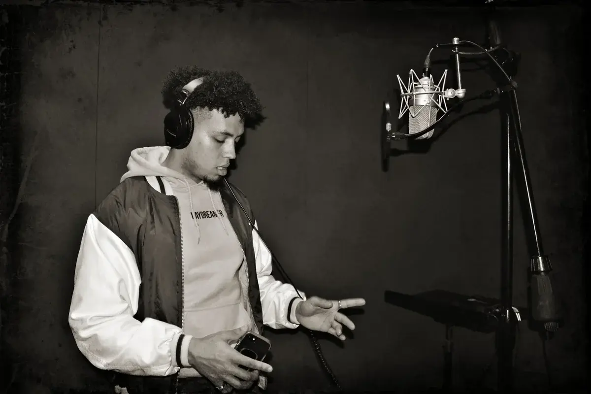 A young rapper recording vocals in a studio while wearing headphones.