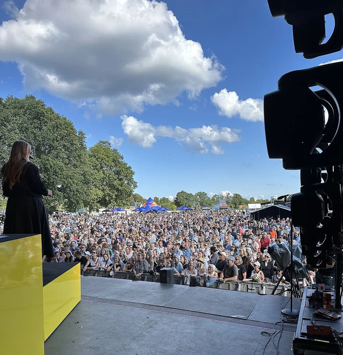 A performer on an outdoor stage facing a large festival crowd.