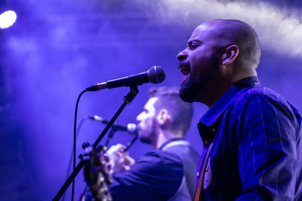 Two musicians singing on a stage lit in purple.