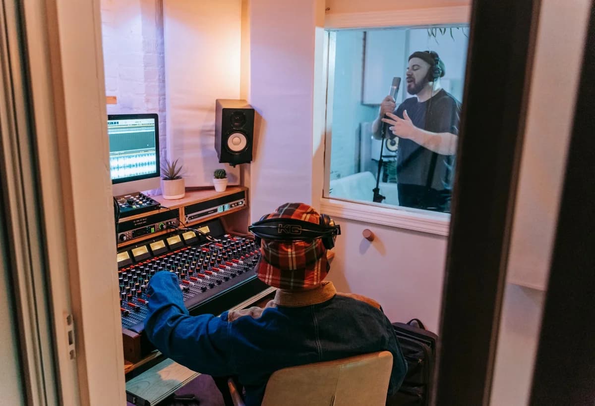 Sound engineer at mixer console and musician singing into microphone in recording studio