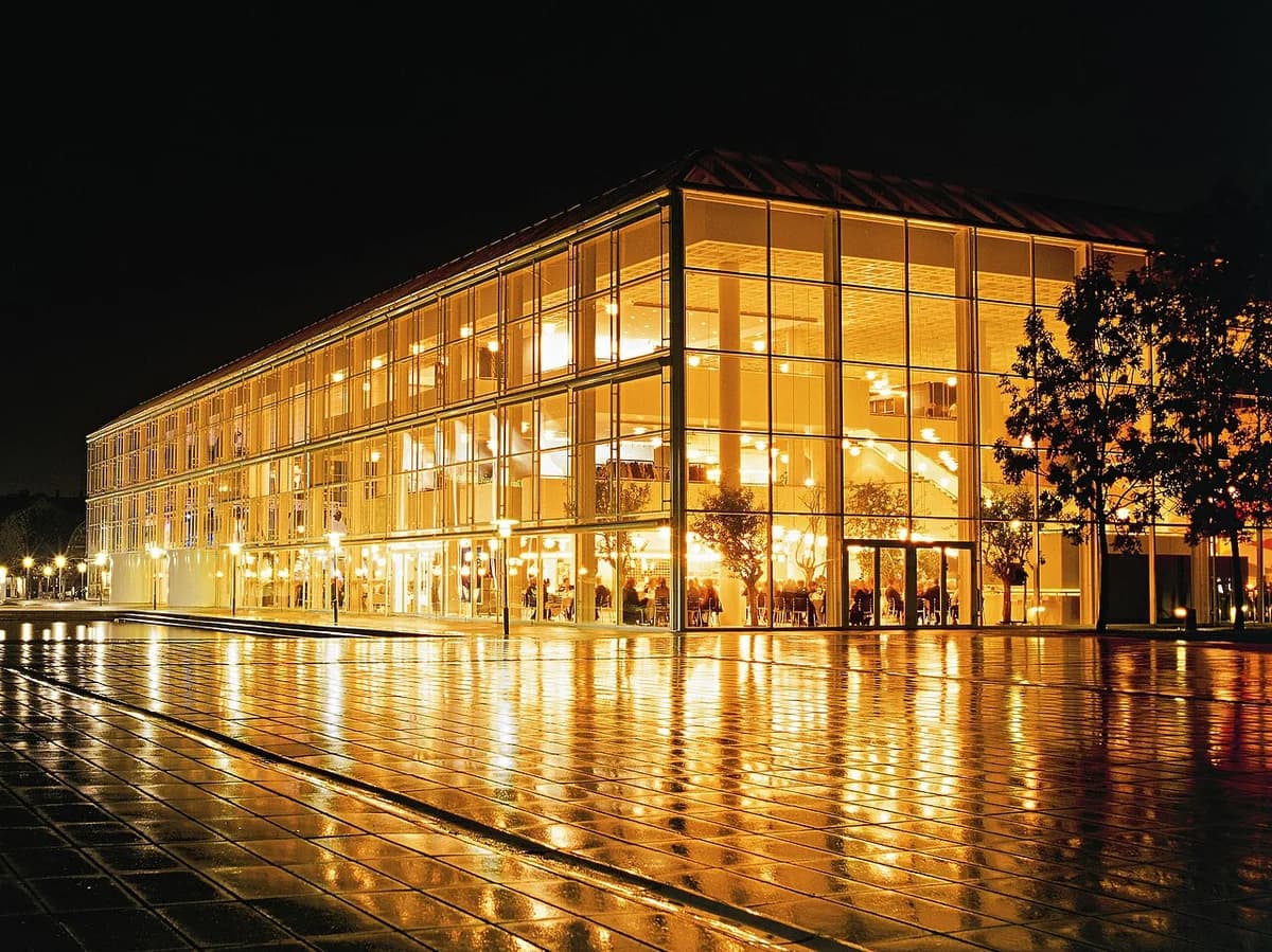 Night view of the illuminated Musikhuset Aarhus building with reflections on the wet ground.