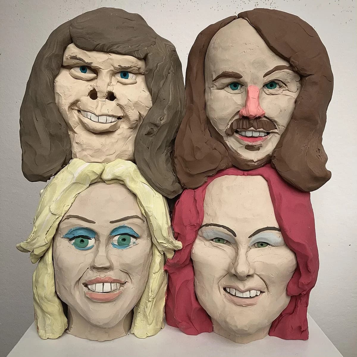 Four sculpted ABBA-related heads arranged in a square composition.