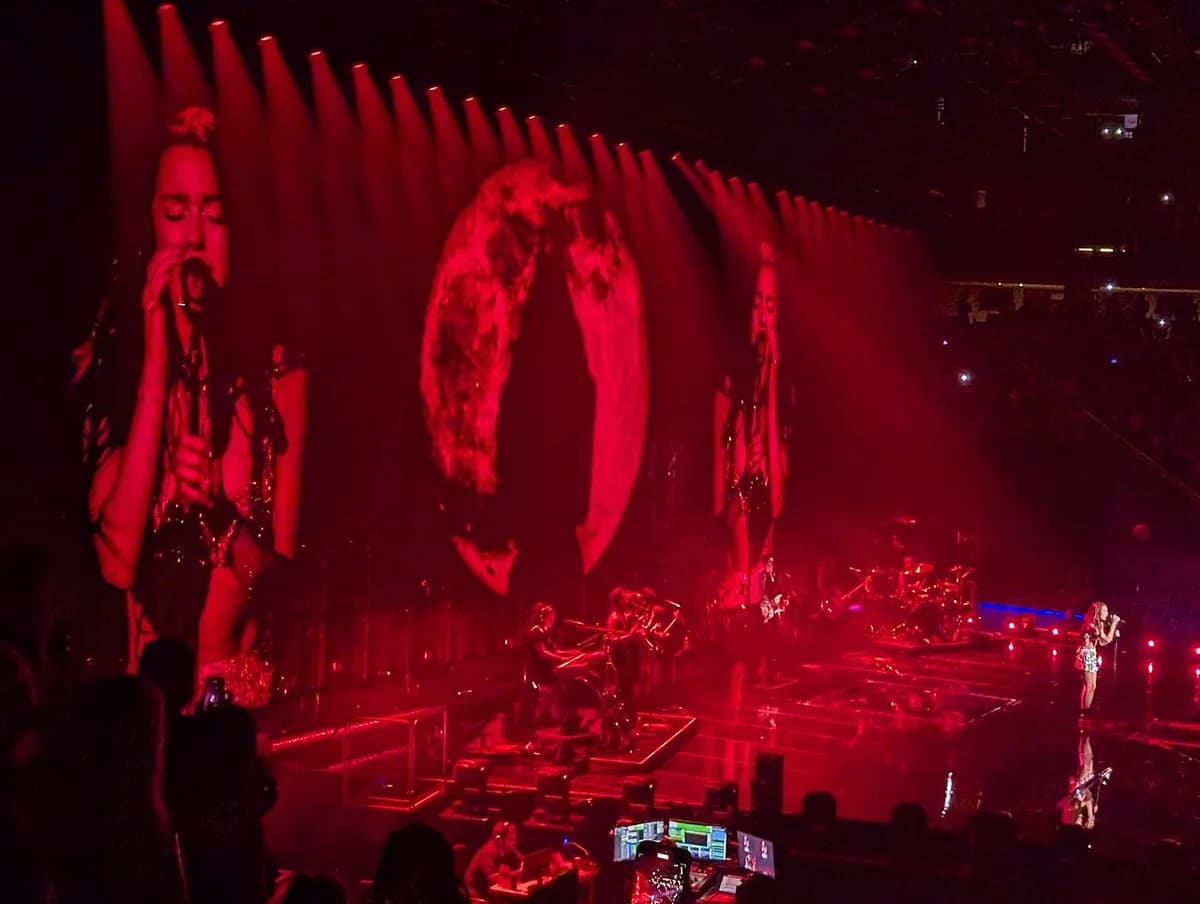 Olivia Rodrigo singing on stage with red lighting and large screen visuals