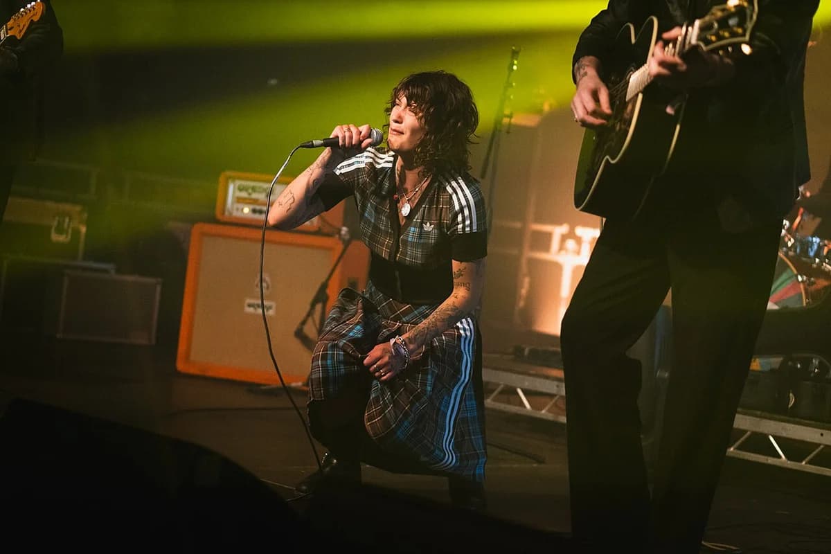A singer performs onstage with a guitarist beside them under green lights.