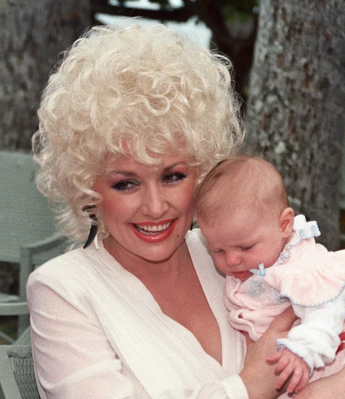 Dolly Parton holding a baby and smiling outdoors
