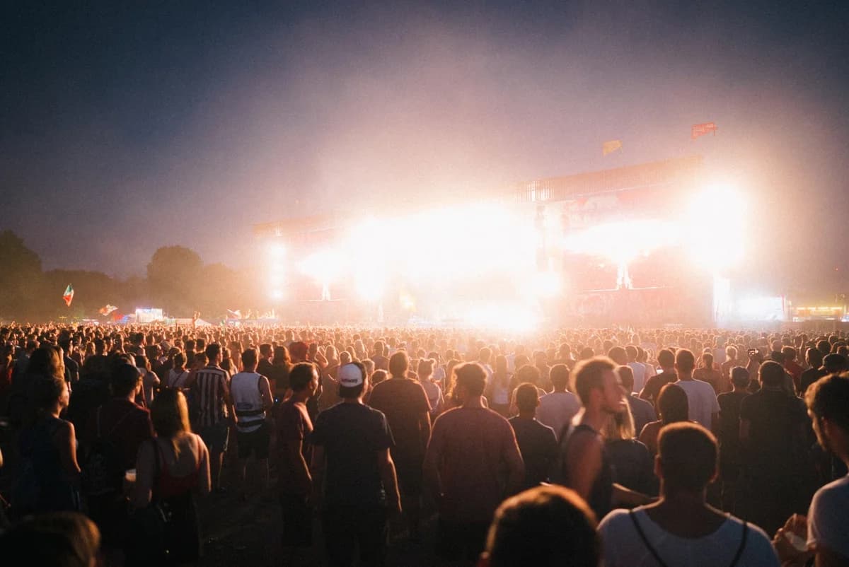 A large nighttime crowd watches a brightly lit outdoor concert stage.