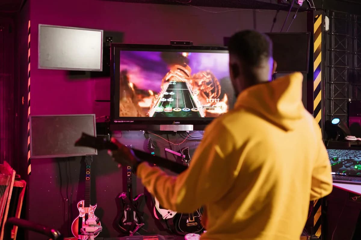 Man in a yellow hoodie playing Guitar Hero indoors