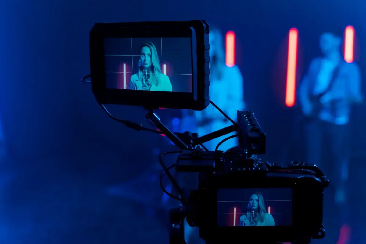 Camera monitors showing a blonde singer holding a microphone in a blue and red lit studio.