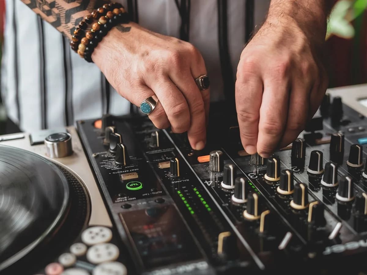 Close-up of tattooed hands operating a DJ mixer.