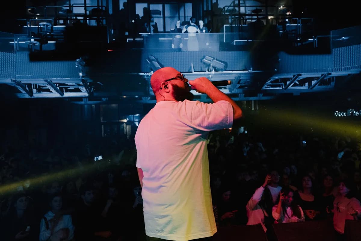 A Black rapper performs on stage under colorful lights in front of a crowd.