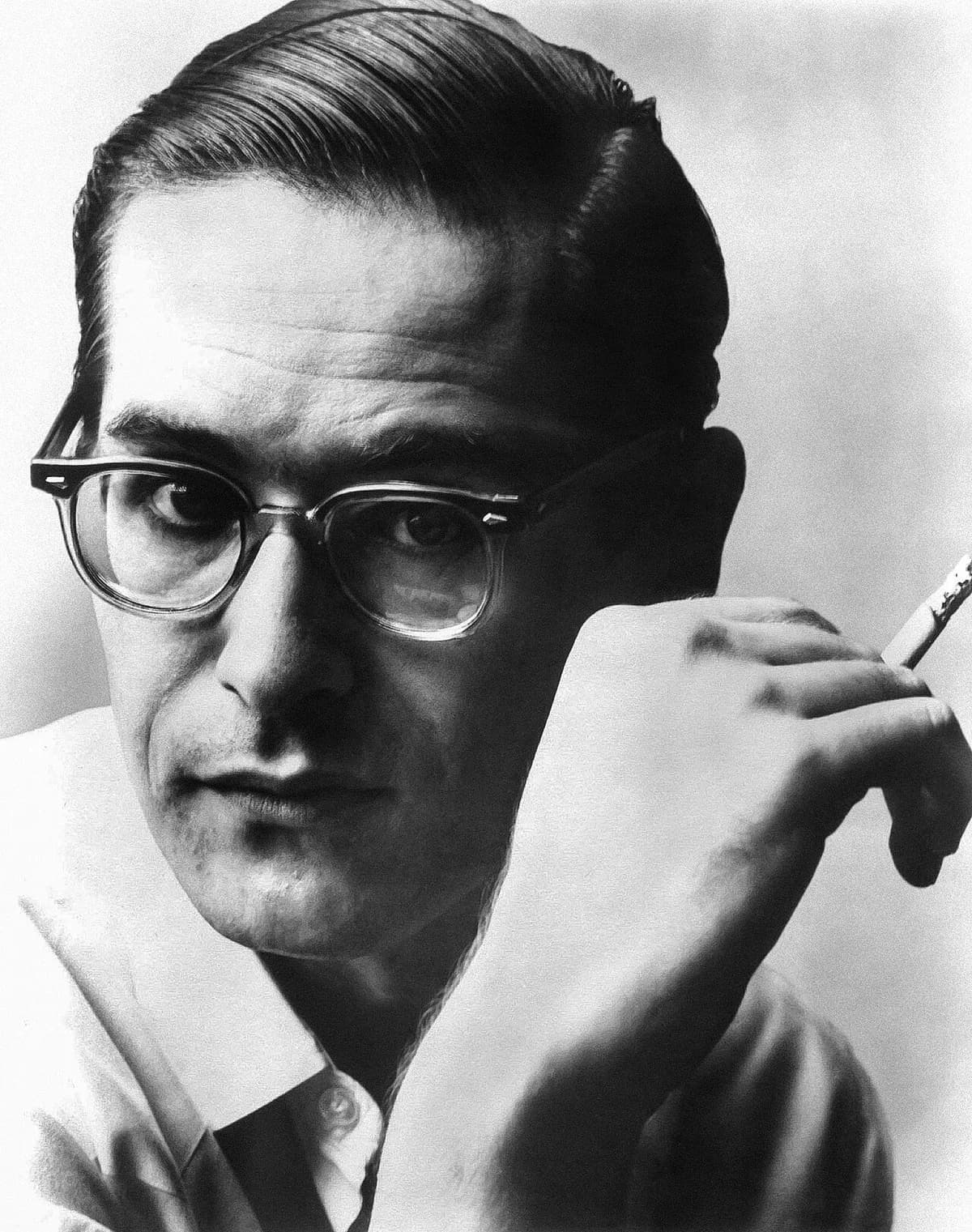 Black-and-white portrait of Bill Evans wearing glasses and holding a cigarette.