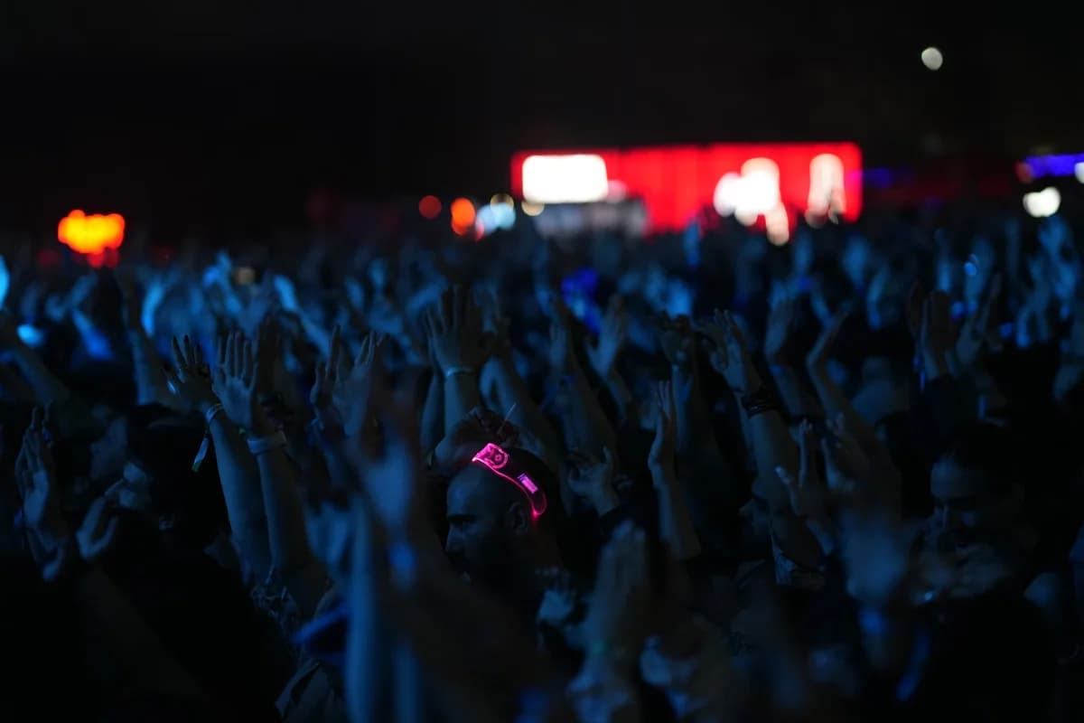 Crowd at a night concert with hands raised under blue lighting.