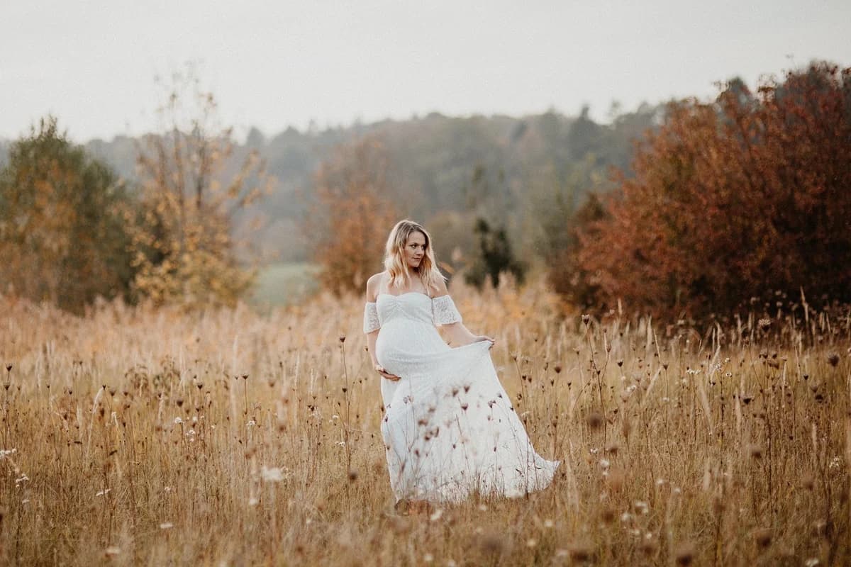 A pregnant woman in a white dress standing in a field.