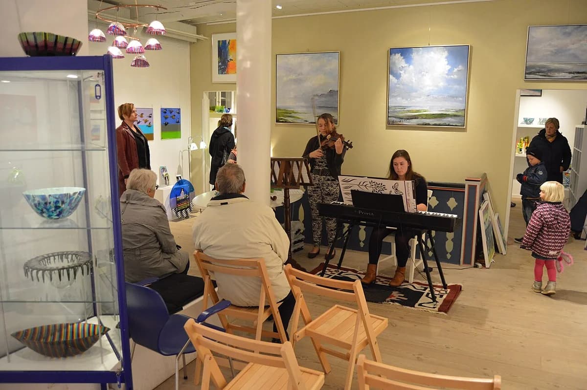 A small indoor concert in an art gallery with a violinist, keyboard player, and seated audience.