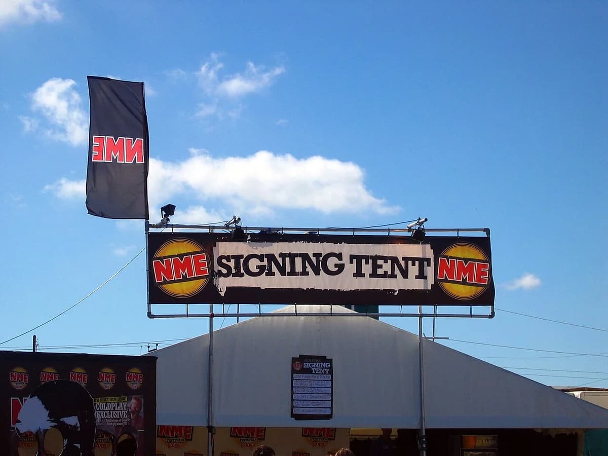 An NME signing tent at an outdoor music festival under a blue sky.