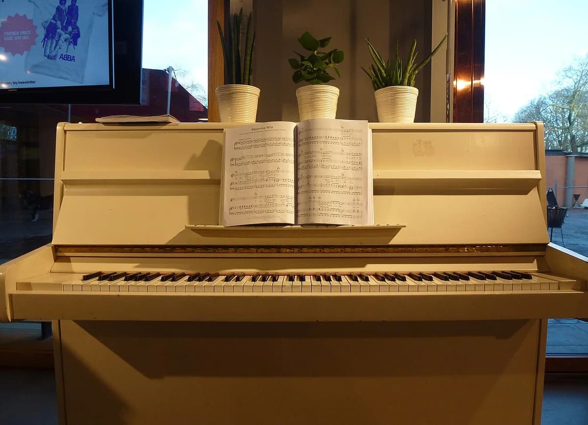 A white piano display with sheet music and potted plants at ABBA The Museum.