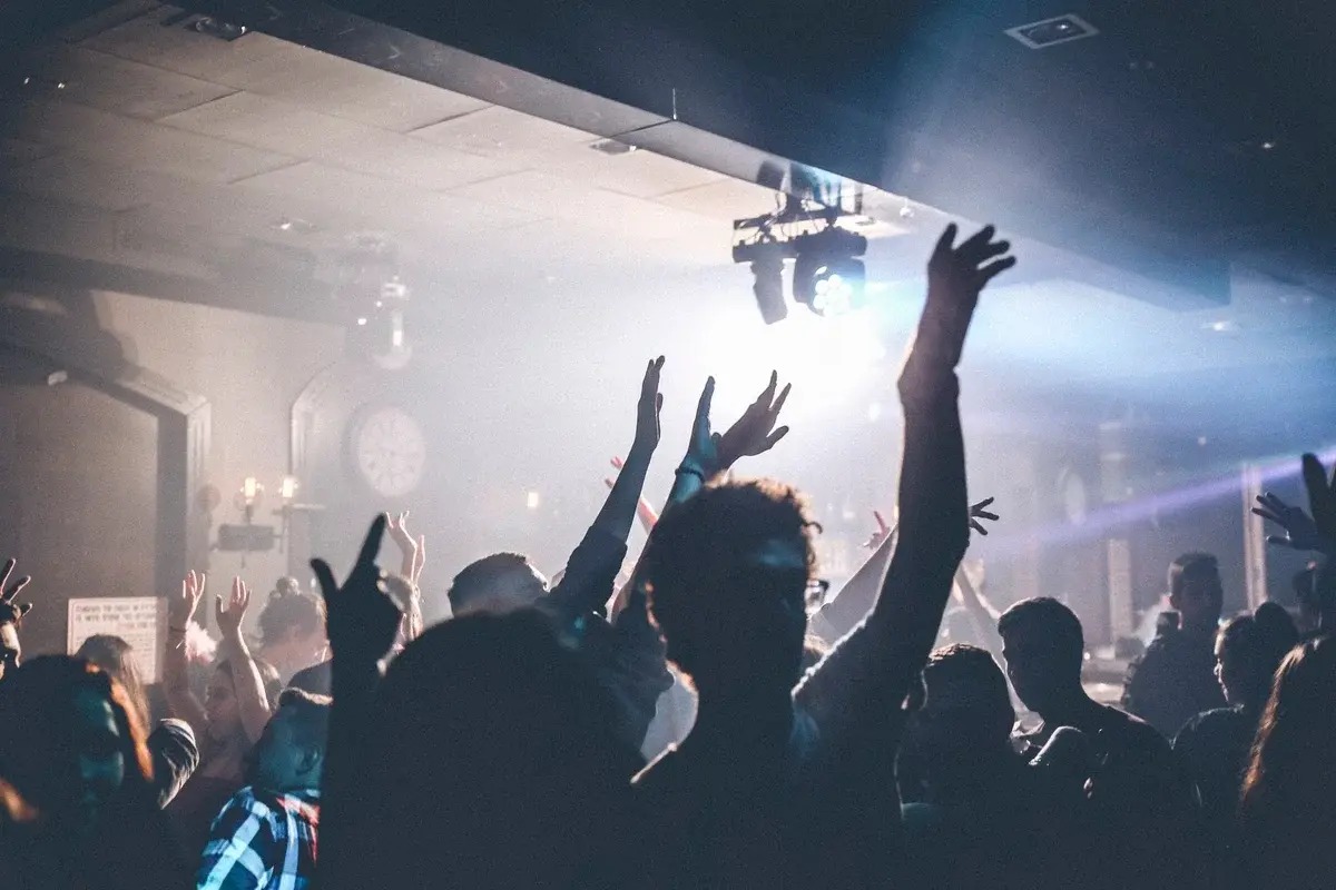 Crowded nightclub dance floor with people dancing under bright lights.