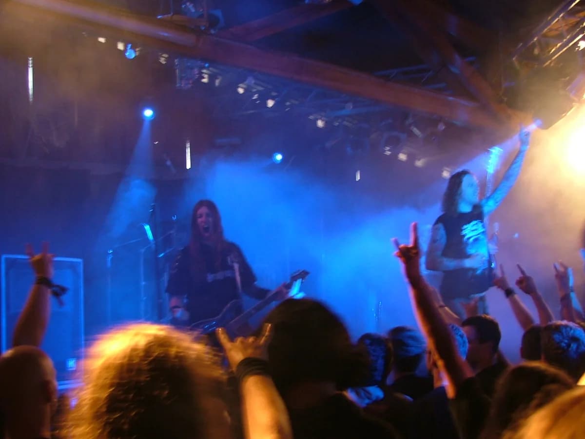 A metal band performing live on stage with audience hands raised in front.