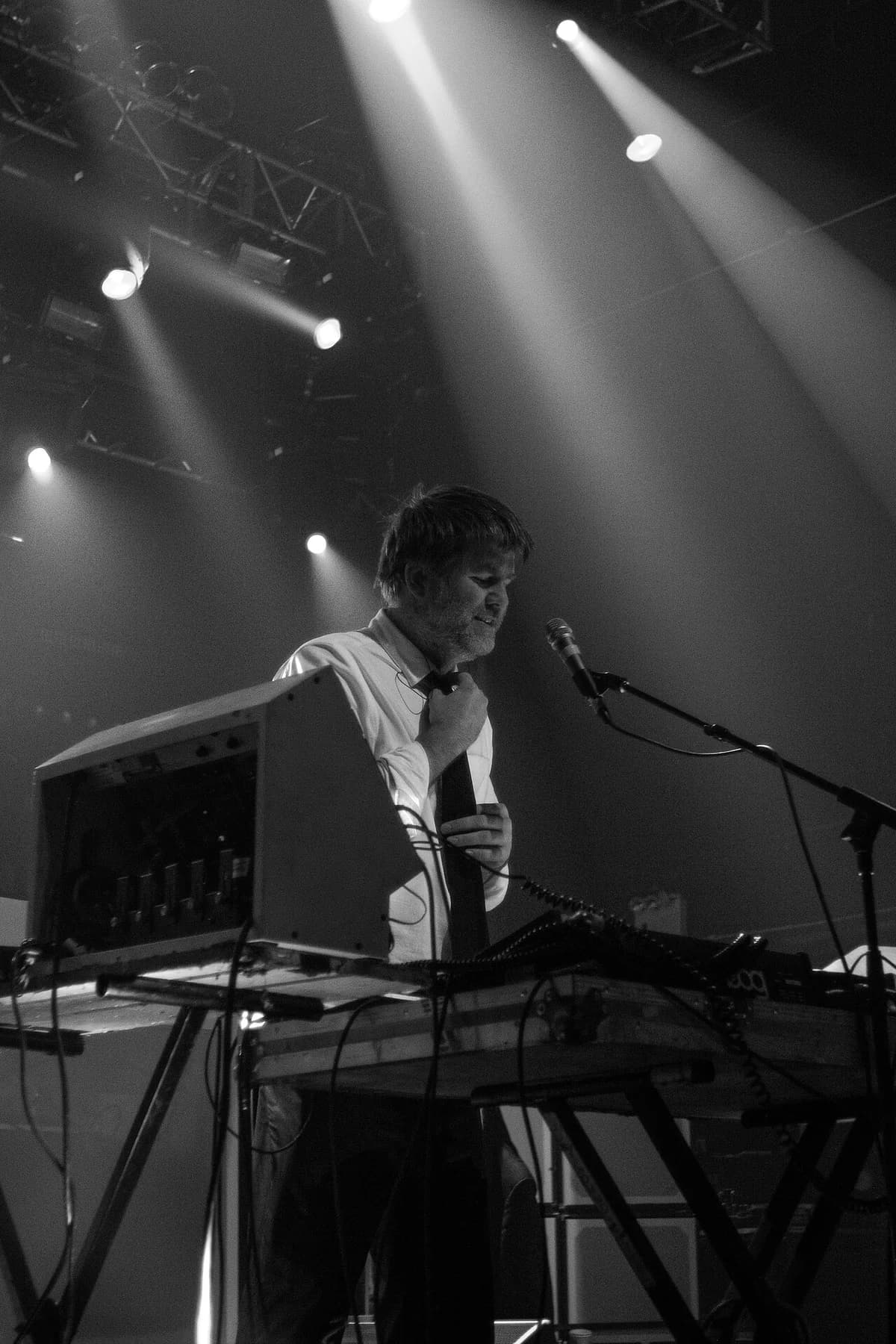James Murphy performing onstage with LCD Soundsystem under stage lights.
