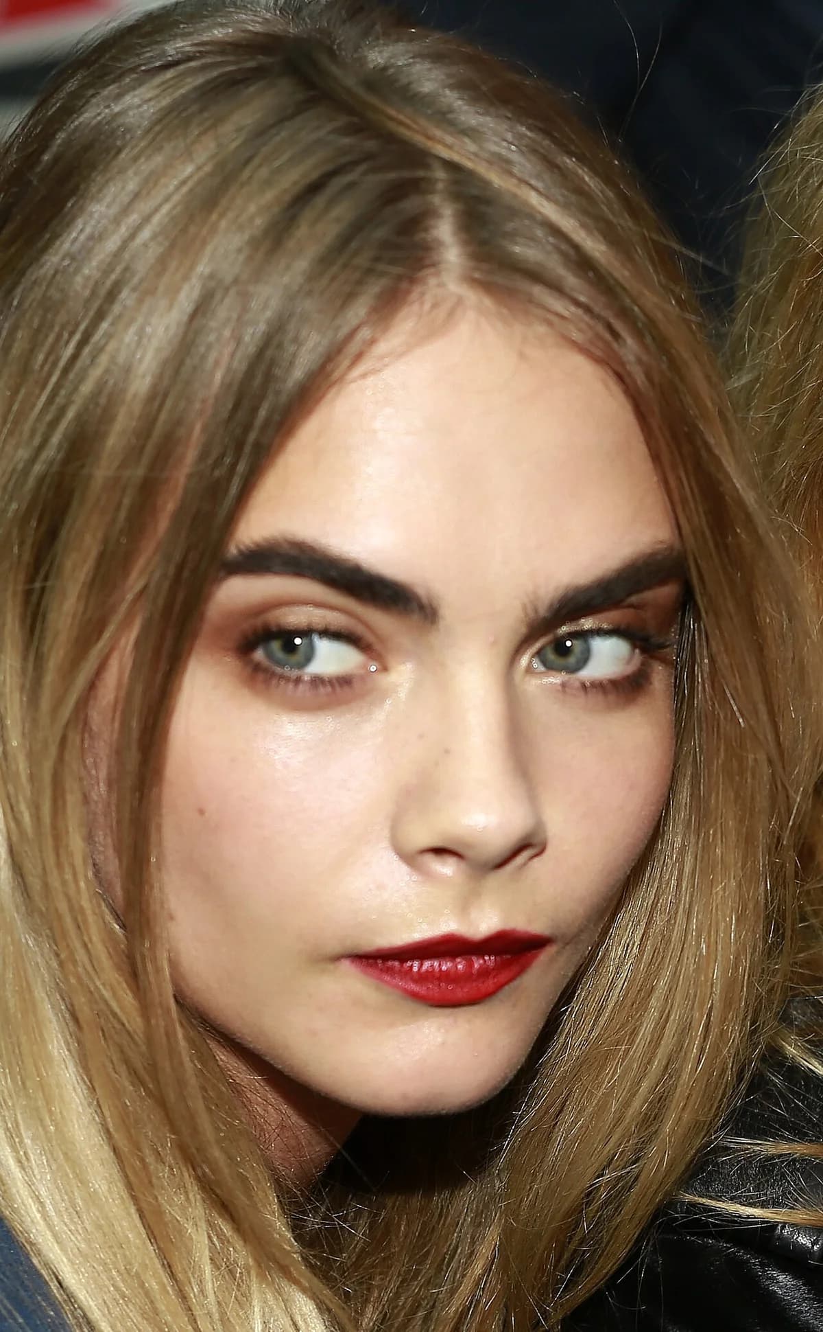 Close-up of a blonde woman with bold makeup at a fashion show.