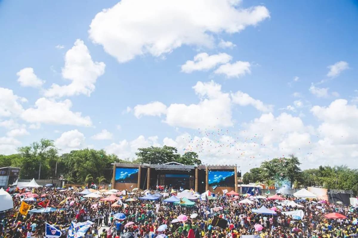 Crowded outdoor festival with colorful umbrellas and a stage under a blue sky