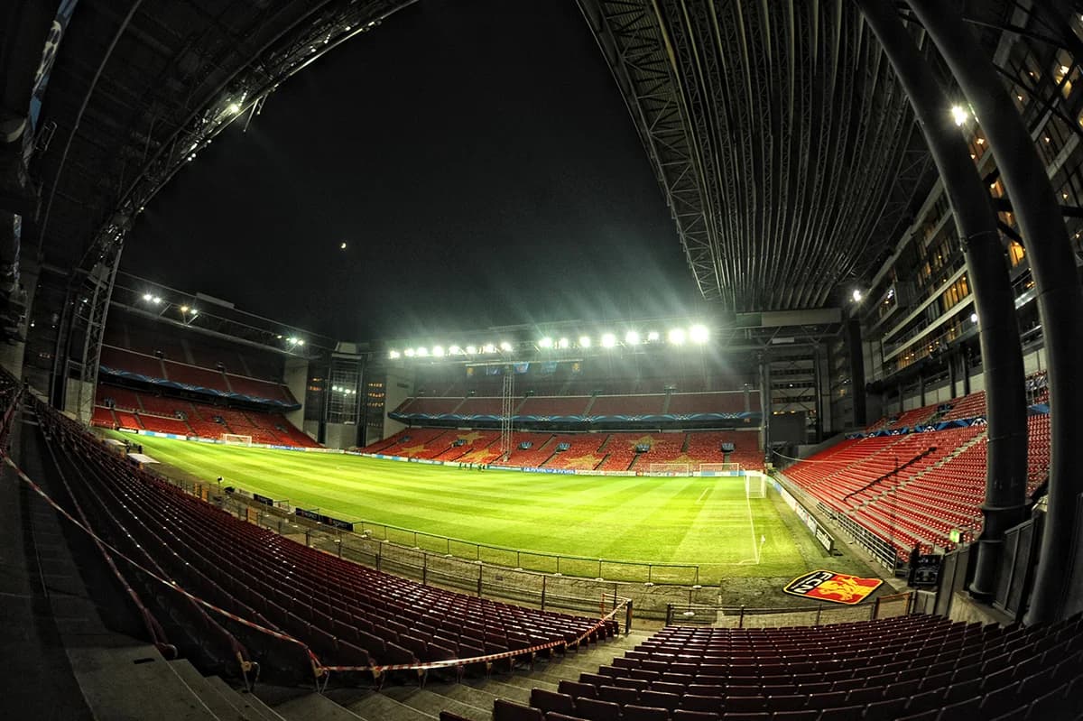 Empty football stadium illuminated at night with red seats and green pitch