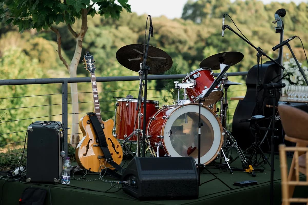 An outdoor stage with a drum kit, guitar, and amplifier in a green natural setting.