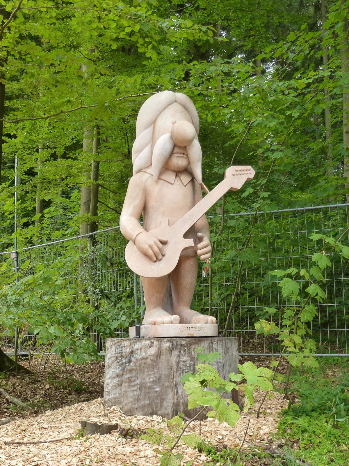 Wooden statue of a musician holding an electric guitar in a forest