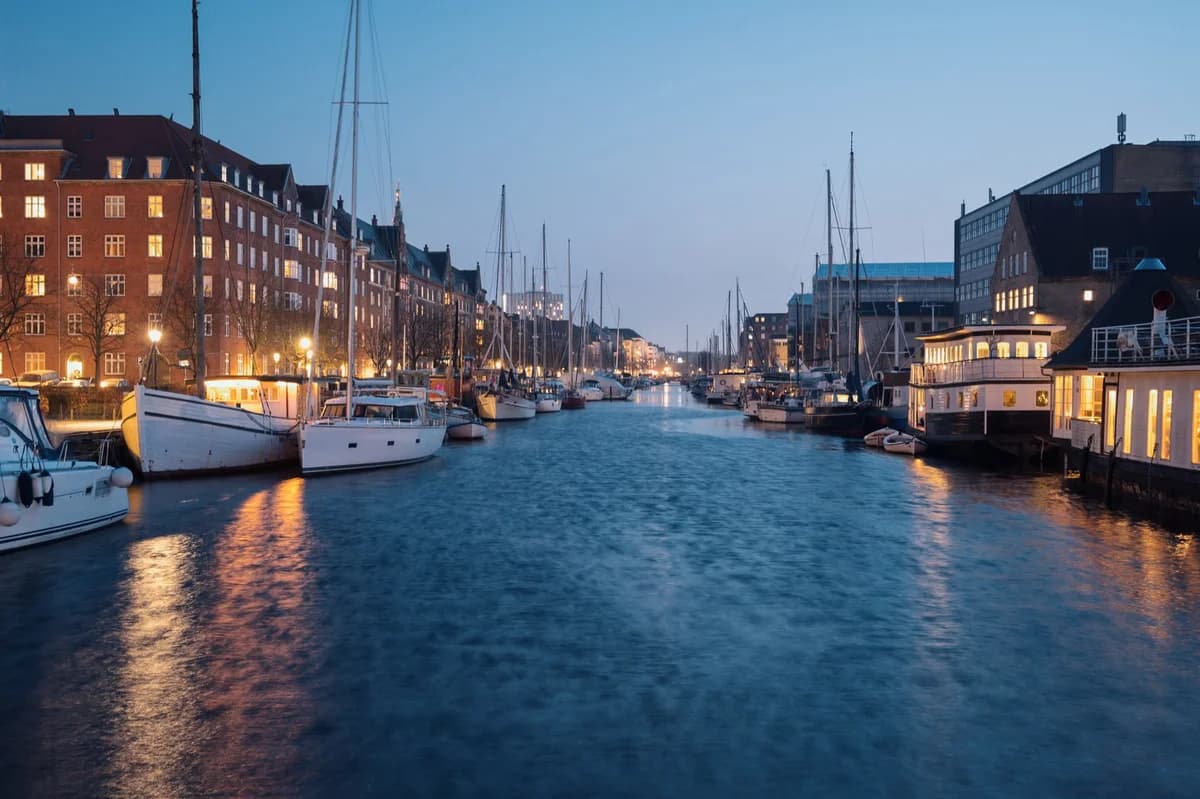 Night view of Nyhavn in Copenhagen with boats and lit buildings along the canal.