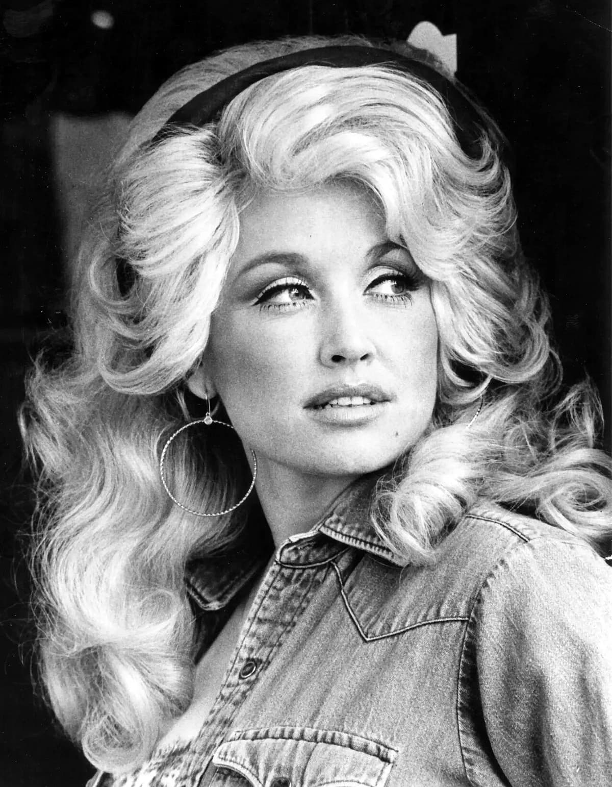 Black-and-white portrait of Dolly Parton in 1977 with big blonde hair and hoop earrings.