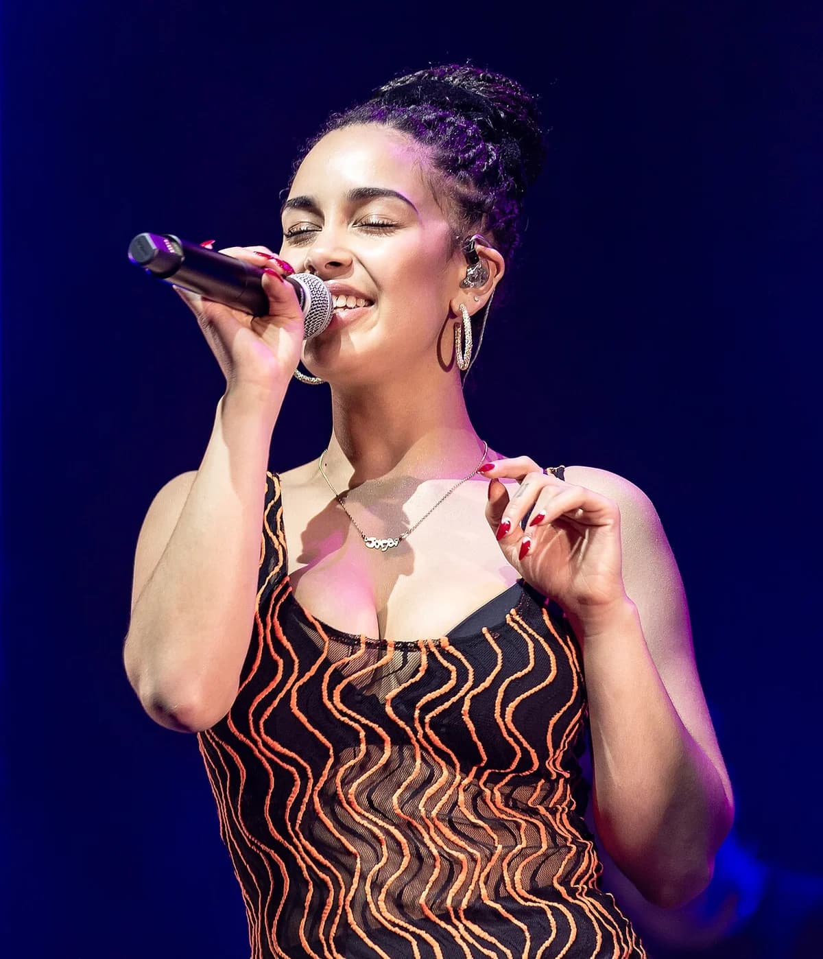 Jorja Smith singing on stage with eyes closed and microphone in hand
