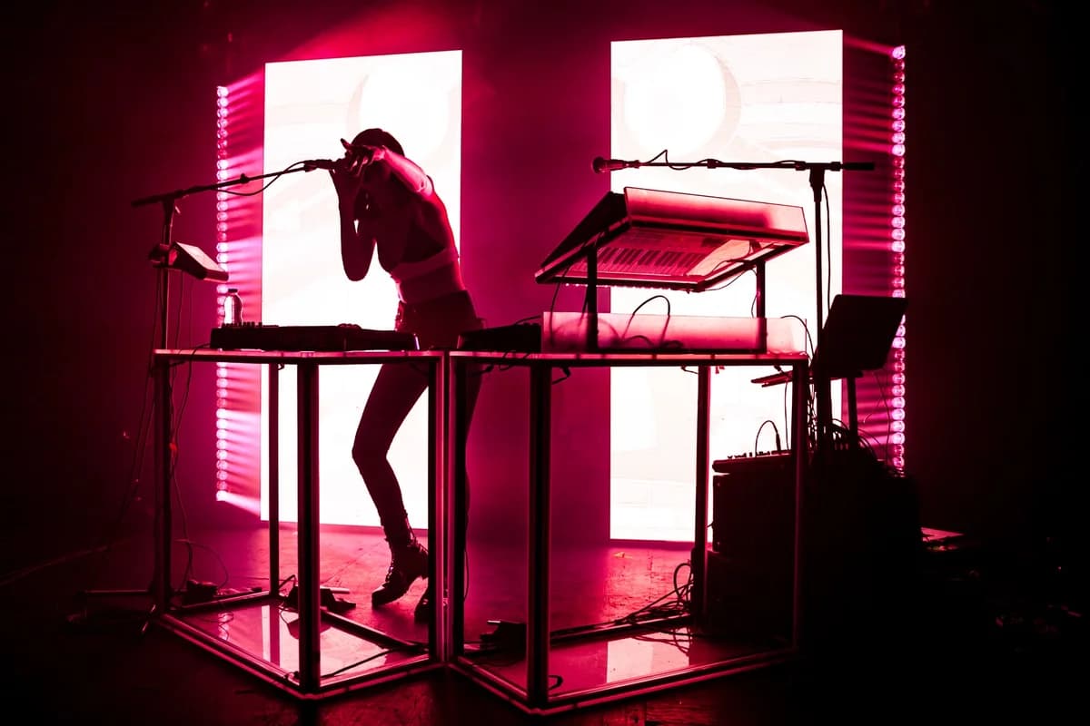 Silhouetted DJ performing on stage under bright pink and white lights