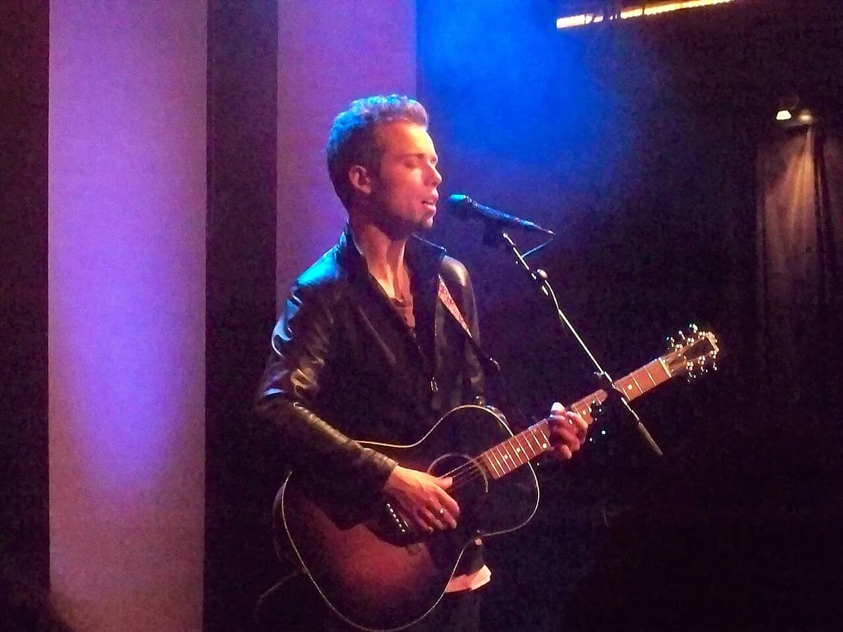 Danish singer-songwriter Mads Langer performing with a guitar on stage.