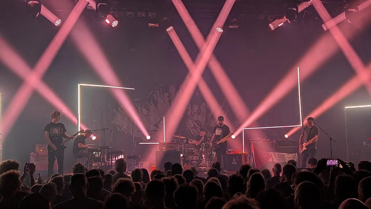 A band performs onstage under pink lights in front of an audience.