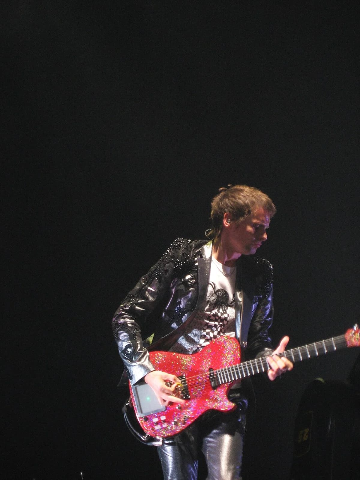 Matthew Bellamy playing a red glitter electric guitar on stage.
