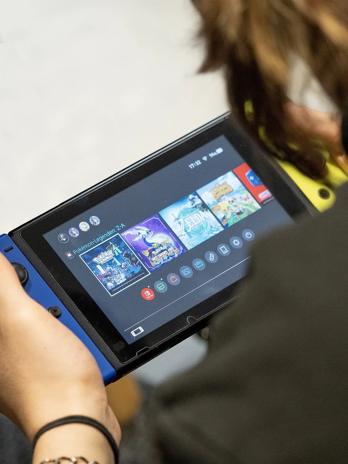 Person using a Nintendo Switch handheld with Pokémon games visible on the screen.