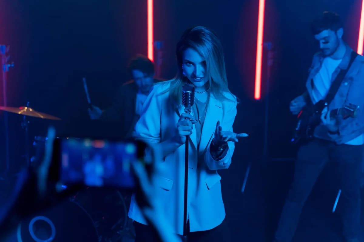 Female singer holding a microphone on stage with a live band under neon lights.