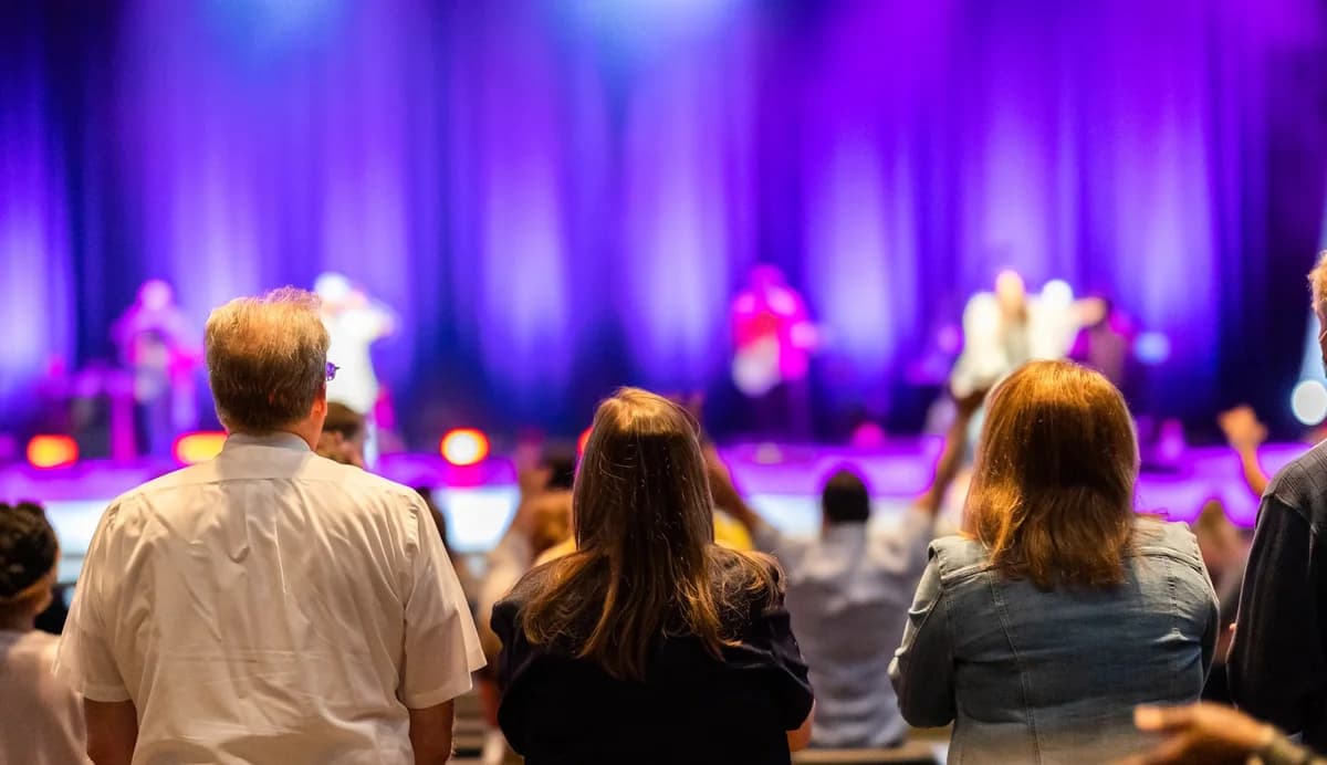 People seen from behind watching a brightly lit concert stage.