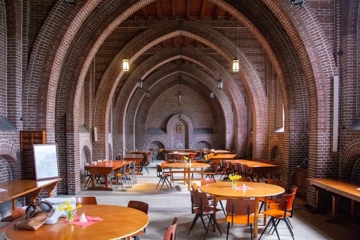 An empty dining hall with brick arches and set tables.